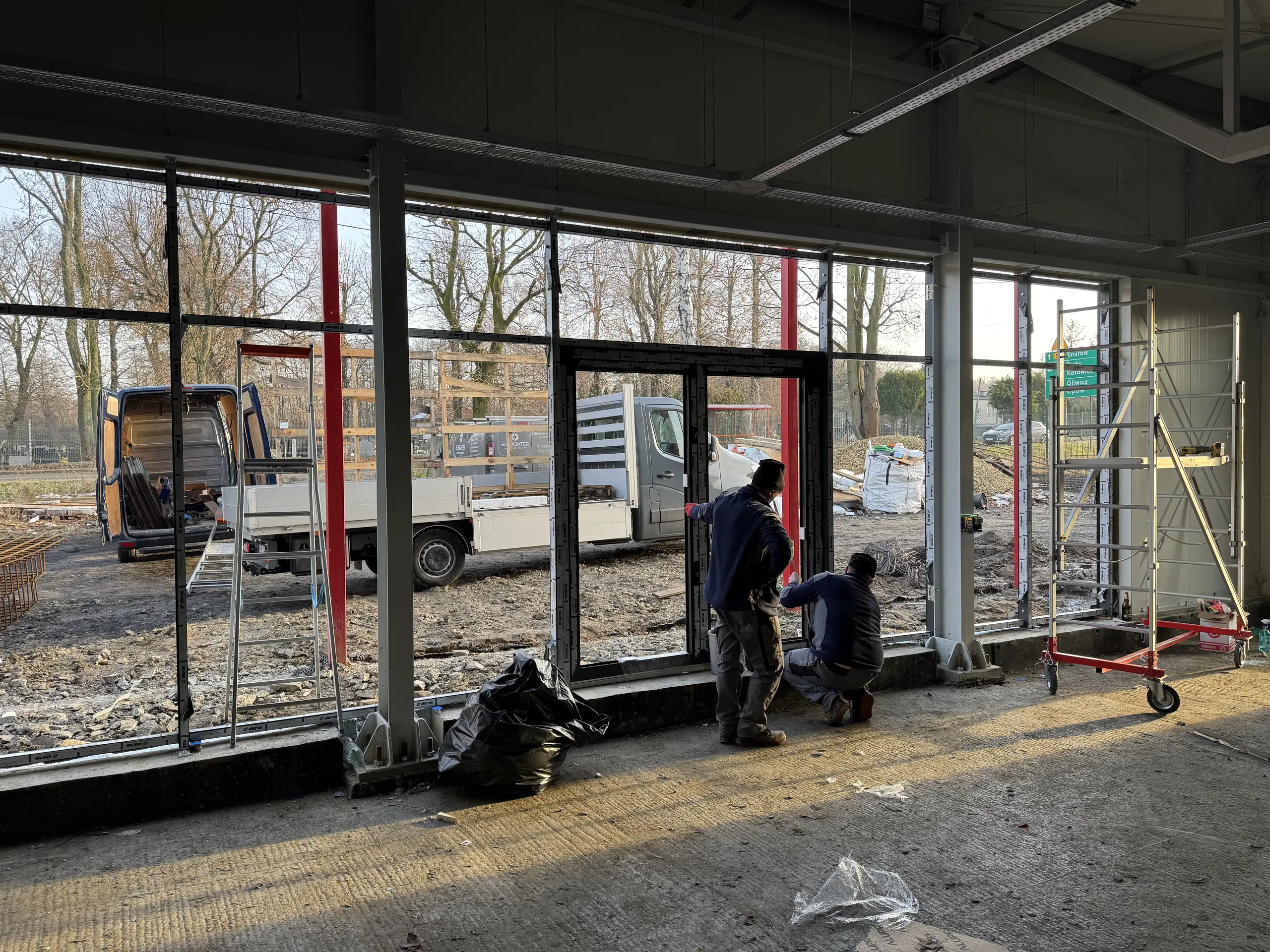 Dwóch monterów montujących aluminiowe drzwi w surowym wnętrzu Montaż drzwi