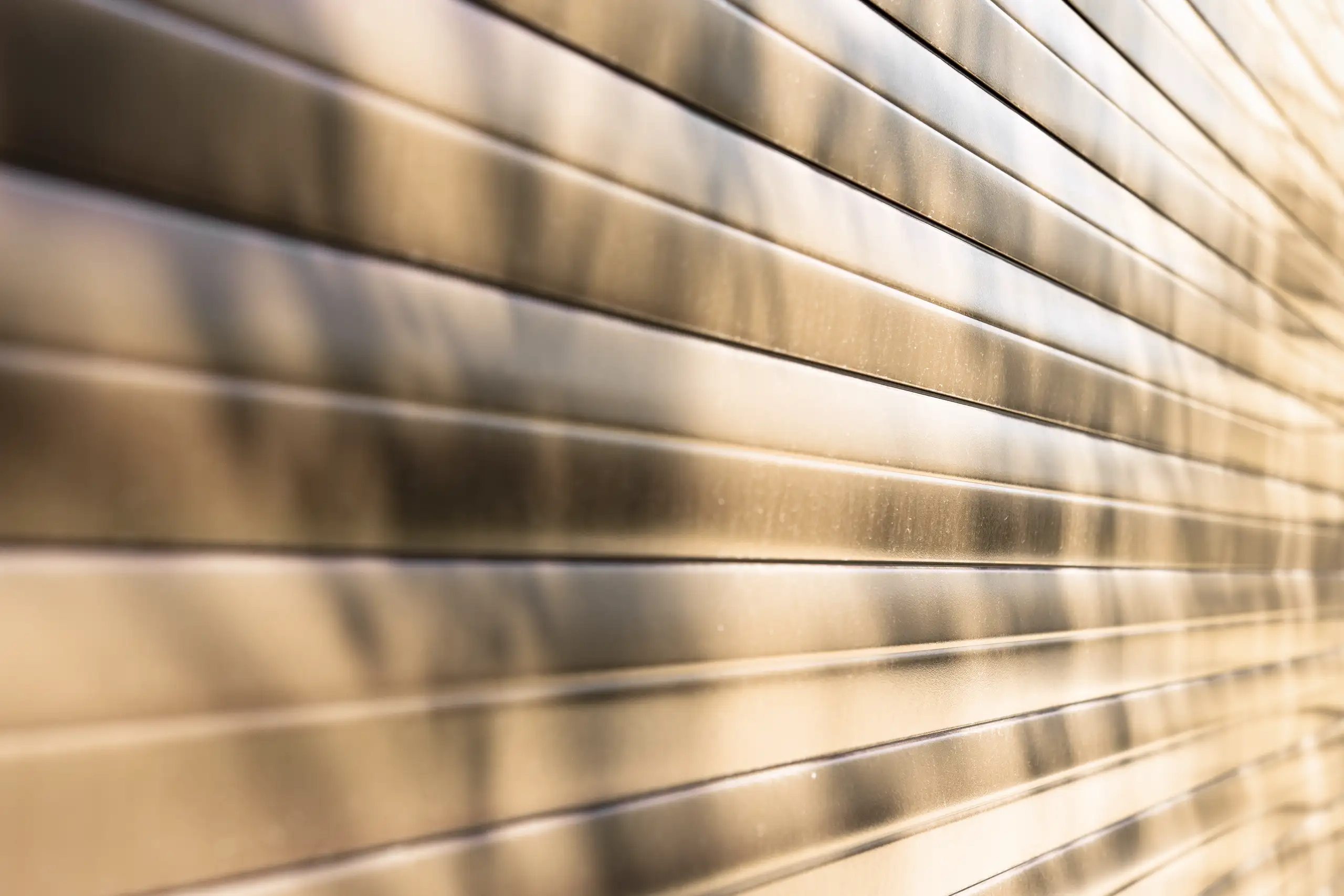 Zbliżenie na zamkniętą aluminiową bramę rolowaną z poziomymi lamelami i ciepłymi cieniami